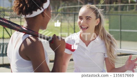 Smiling and talking tennis players standing near net on green court, with racket headband and fence 135657669