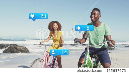 Friends pedaling pink, green bikes on beach with rocky outcrops, with blue notification icons Friends pedaling pink, green bikes on beach with rocky outcrops, with blue notification icons 135657673