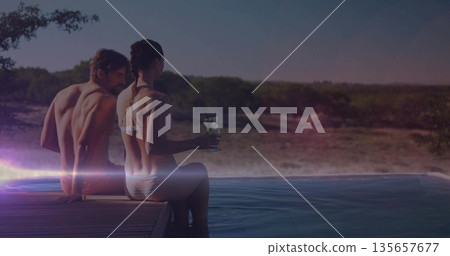 Sitting couple in swimwear holding cocktail glass on wooden pool deck at infinity pool, copy space Sitting couple in swimwear holding cocktail glass on wooden pool deck at infinity pool, copy space 135657677