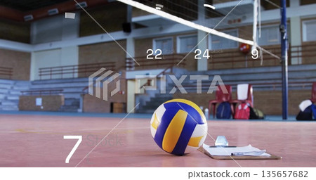 Lying volleyball beside clipboard and pen on gymnasium court, with net posts and red chairs 135657682