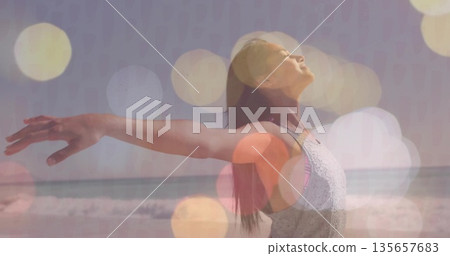 Stretching arms woman in sleeveless tank top under bokeh effect at sandy shoreline, waves rolling 135657683