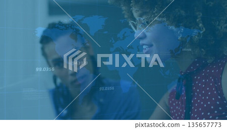 Analyzing laptop data two colleagues wearing red blouse, eyeglasses at desk with world map overlay 135657773