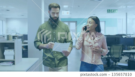 Walking colleagues in business attire in office, carrying documents while speaking into smartphone Walking colleagues in business attire in office, carrying documents while speaking into smartphone 135657810