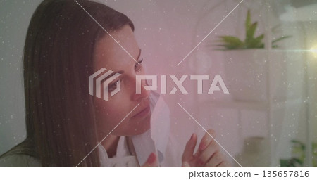 Woman in light blouse applying sheet mask in home vanity, with white shelf and green plants Woman in light blouse applying sheet mask in home vanity, with white shelf and green plants 135657816
