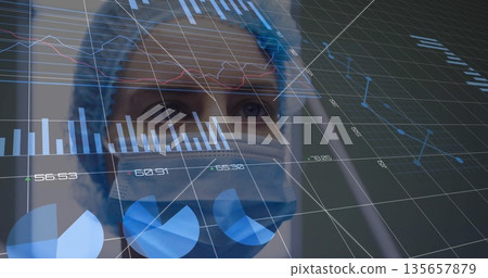 Nurse wearing surgical cap mask and scrubs interpreting charts in medical lab, glass data overlay 135657879