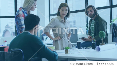 Collaborating coworkers discussing around desk in open-plan office with plans and coffee mugs 135657880