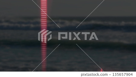 Shining narrow vertical red beam reflecting off ocean waves at seaside at night, faint horizon line 135657904