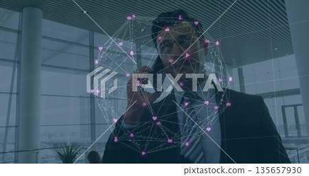 Holding man in suit speaking on smartphone in modern lobby, with network globe and metallic columns 135657930