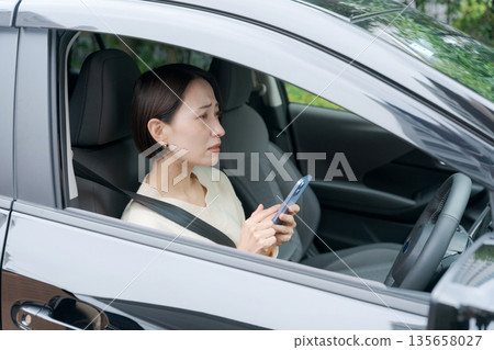 A woman looking at her smartphone in the driver's seat A woman looking at her smartphone in the driver's seat 135658027