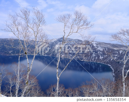 View of Lake Mashu over the remaining snow-covered birch trees from Lake Mashu No. 1 Observation Deck View of Lake Mashu over the remaining snow-covered birch trees from Lake Mashu No. 1 Observation Deck 135658354