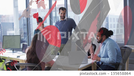 Five team members reviewing digital charts and leaning over desk in office meeting, with laptops 135658864