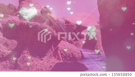 Climbing girl in striped suit pulling on granite boulder in shallow water, with heart-shaped lights Climbing girl in striped suit pulling on granite boulder in shallow water, with heart-shaped lights 135658950