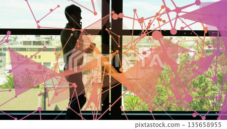 Talking woman holding smartphone and gesturing by office window, with abstract network overlay 135658955
