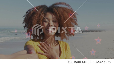 Reaching woman in yellow polka dot dress guiding viewer hand on shoreline, with pink star overlay 135658970