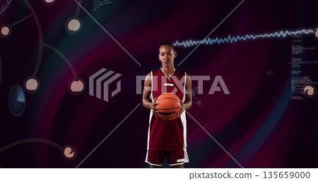 Standing female basketball player wearing crimson and white jersey in studio, holding basketball Standing female basketball player wearing crimson and white jersey in studio, holding basketball 135659000