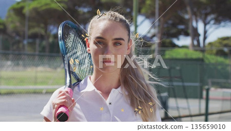 Standing woman wearing white shirt holding pink-gripped racket on tennis hardcourt, with windscreen 135659010