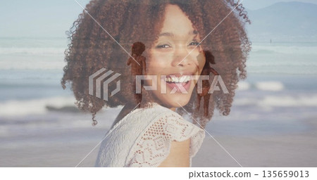Smiling mother with curly hair walking with children on sandy beach, with swimsuits and ocean waves 135659013