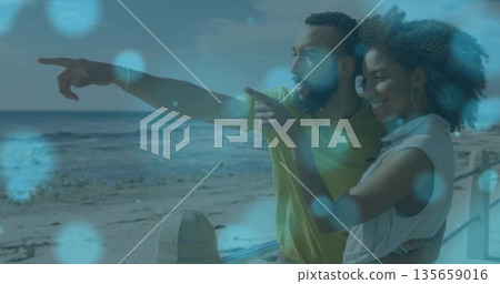 Leaning couple pointing toward calm ocean at beachfront promenade with railing, copy space Leaning couple pointing toward calm ocean at beachfront promenade with railing, copy space 135659016