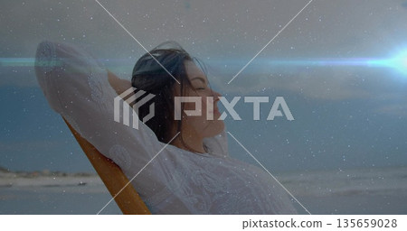 Reclining woman leaning back with hands behind head on lounge chair on sandy beach, copy space 135659028