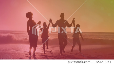 Jumping family of four holding hands barefoot along shoreline at dusk, wet sand waves footprints 135659034