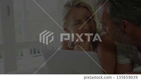 Reclining couple leaning toward each other and chatting in lounging area by balcony, with laptop 135659039