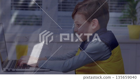 Boy wearing yellow vest typing on laptop at kitchen table, with glass of orange juice Boy wearing yellow vest typing on laptop at kitchen table, with glass of orange juice 135659040