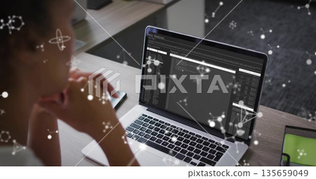 Reviewing mid adult woman examining terminal windows on laptop at workspace, with network overlays 135659049