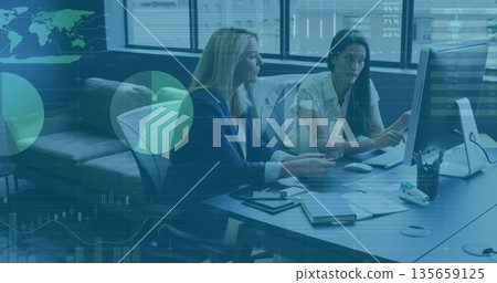 Pointing businesswomen collaborating on computer monitor at office desk, with scattered notebooks 135659125