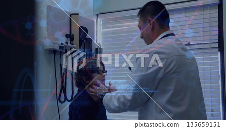 Asian doctor in white coat holding child's jaw and checking throat in exam room with stethoscope Asian doctor in white coat holding child's jaw and checking throat in exam room with stethoscope 135659151