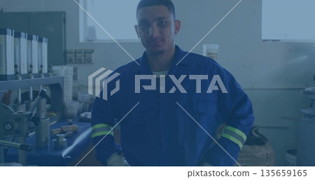 Operating Hispanic machinist wearing striped coverall handling lathe in workshop, with metal parts Operating Hispanic machinist wearing striped coverall handling lathe in workshop, with metal parts 135659165