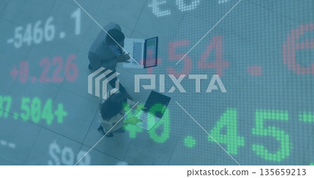 Walking business professionals checking market data on laptops across office lobby, stock overlay 135659213