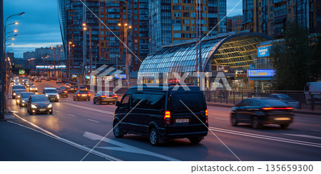 Black van driving on a busy city street at dusk, with modern buildings and illuminated storefronts visible in the background Black van driving on a busy city street at dusk, with modern buildings and illuminated storefronts visible in the background 135659300