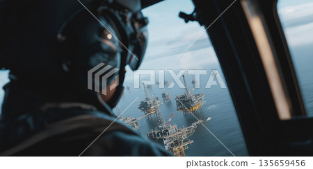 Helicopter pilot wearing headset views offshore oil rigs from cockpit window, multiple platforms visible in the ocean under a cloudy sky 135659456