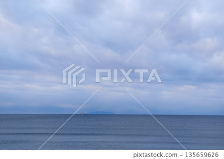 A calm sea under a cloudy sky and a large ship anchored offshore A calm sea under a cloudy sky and a large ship anchored offshore 135659626