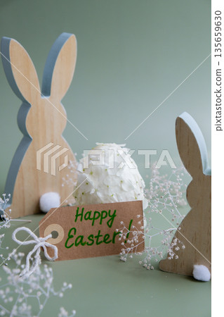 Greeting card with text HAPPY EASTER Creative Easter egg shape made of white lilac spring petals flowers. Responsible holidays decoration wooden rabbit bunny decor. Present gift idea Minimal holiday 135659630