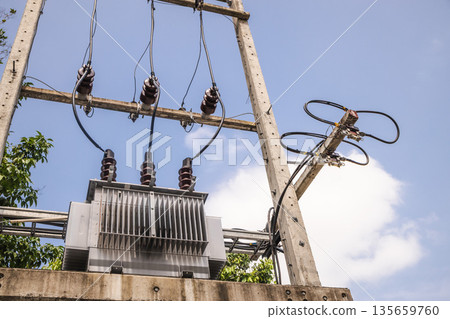 Power transformer and high voltage cables mounted on concrete utility structure in tropical Thailand, clear blue sky and green trees in background Power transformer and high voltage cables mounted on concrete utility structure in tropical Thailand, clear blue sky and green trees in background 135659760
