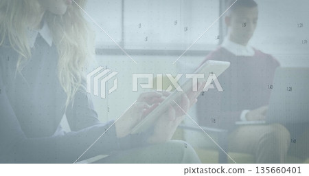 Woman in sweater tapping tablet in office lounge chairs by windows, typing on laptop data overlay Woman in sweater tapping tablet in office lounge chairs by windows, typing on laptop data overlay 135660401