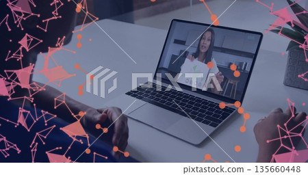 Women in blue shirt and dark top viewing laptop in home office, with printed diagram sheet 135660448