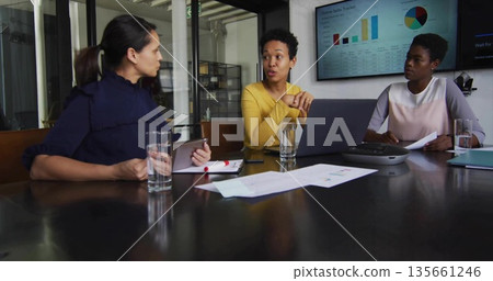 Three businesswomen examining charts and data in conference room with laptop tablet speakerphone Three businesswomen examining charts and data in conference room with laptop tablet speakerphone 135661246