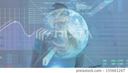 Data analyst wearing teal top tapping stylus on holographic charts in office, with globe hologram 135661267