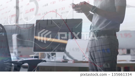 Data analyst wearing gray shirt reviewing charts on monitors in open plan office, copy space 135661334