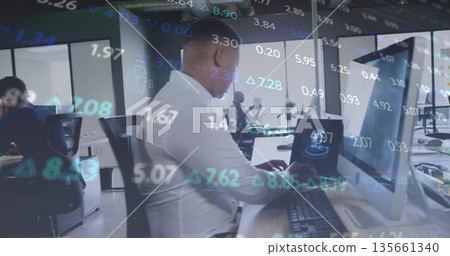 Typing white man reviewing financial data on laptop and desktop in open-plan office, with overlay Typing white man reviewing financial data on laptop and desktop in open-plan office, with overlay 135661340