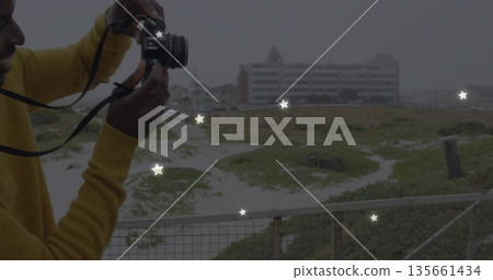 Holding DSLR camera, man in mustard sweater shooting coastal dunes on platform railing, copy space Holding DSLR camera, man in mustard sweater shooting coastal dunes on platform railing, copy space 135661434