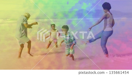 Splashing family wearing beachwear and kicking shallow ocean water on sandy beach, with small waves 135661454