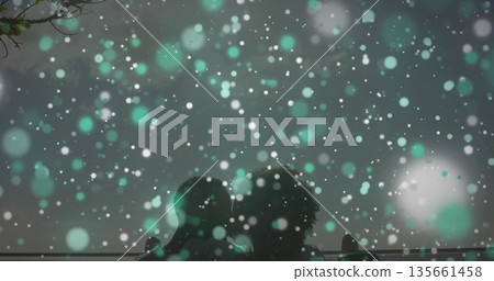 Sitting couple wearing winter coats admiring snow at nighttime park bench, with railing behind Sitting couple wearing winter coats admiring snow at nighttime park bench, with railing behind 135661458