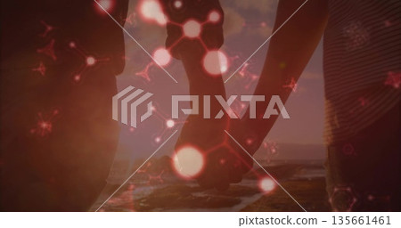 Standing silhouetted couple holding hands on beach at sunset, with floating red molecular graphics Standing silhouetted couple holding hands on beach at sunset, with floating red molecular graphics 135661461