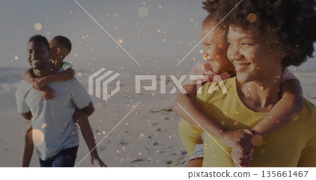 Walking family of four carrying children on backs along sandy beach at sunset, golden bokeh Walking family of four carrying children on backs along sandy beach at sunset, golden bokeh 135661467