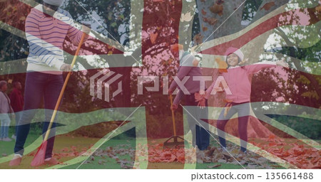 Extended family wearing jackets, knit hats raking, tossing leaves in park with red and metal rakes Extended family wearing jackets, knit hats raking, tossing leaves in park with red and metal rakes 135661488