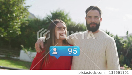 Smiling couple wearing cozy red and cream sweaters posing in garden, with blue notification bubble Smiling couple wearing cozy red and cream sweaters posing in garden, with blue notification bubble 135661501