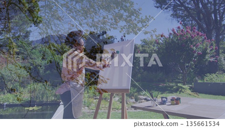 Applying paint African American woman wearing painter's apron at garden easel, with paint jars Applying paint African American woman wearing painter's apron at garden easel, with paint jars 135661534